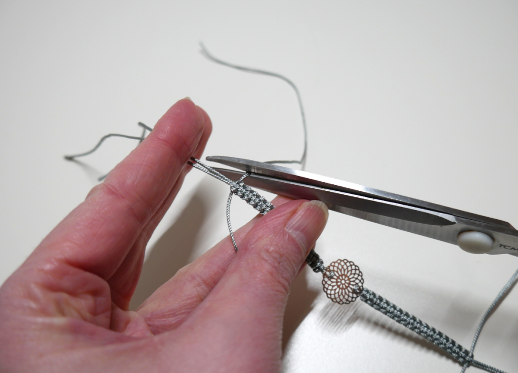 Fäden des Makramee Armbands mit Schere abschneiden