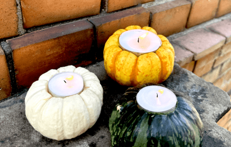 Drei Kürbisse mit angezündetem Teelicht vor einer Hauswand