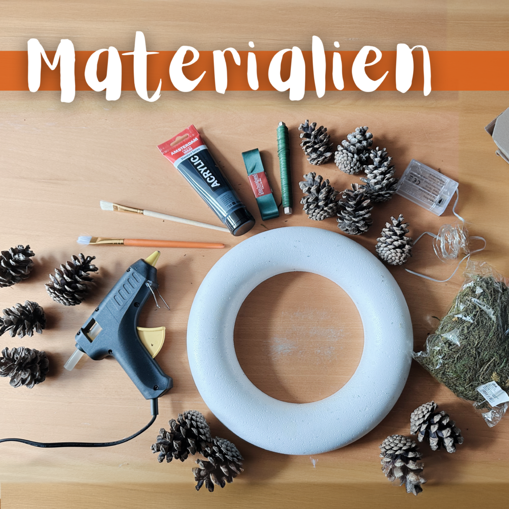 Alle Materialien für den DIY Türkranz liegen bereit: Styroporring, Tannenzapfen, Moos, Acrylfarbe, Pinsel, Heißklebepistole, Band und Draht